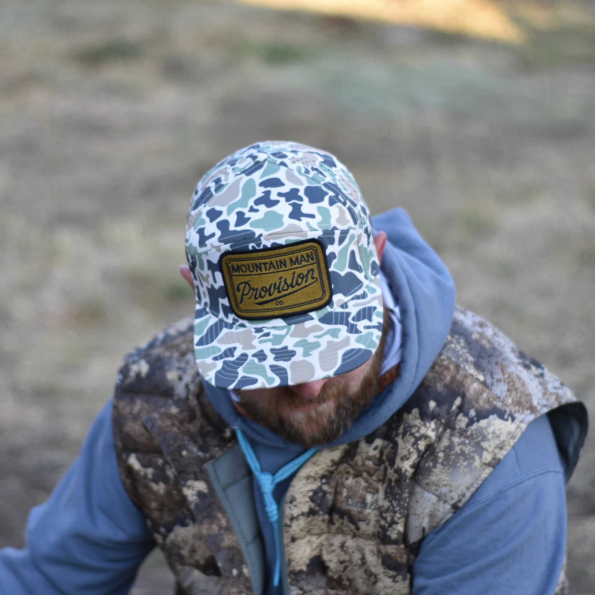 Person wearing a camouflage cap and vest in a natural setting